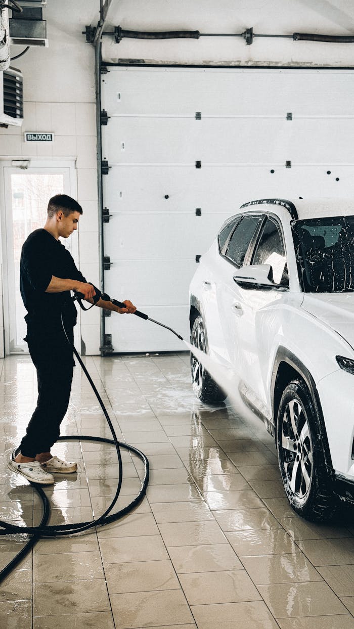 why-choose-us Man using a power washer to clean a car in a garage setting.